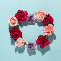 Creative heart arrangement with spring colorful roses and their shadow against pastel blue background. Minimal nature concept. 