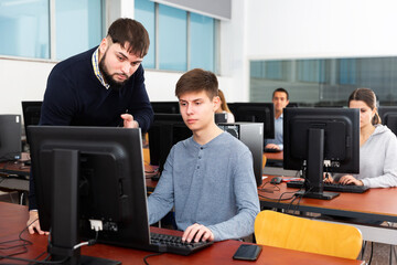 adult serious teacher helping young male student in computer class in university