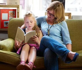 Reading with mom. A cute blonde girl and her mother reading on the couch at home.