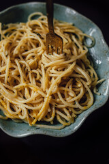 Spaghetti pasta with thyme butter on blue teal ruffled dish on black