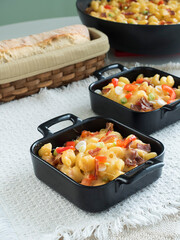 Two individual cast iron serving pans of baked macaroni and cheese on a beige place mat with the skillet and loaf of fresh bread in the background