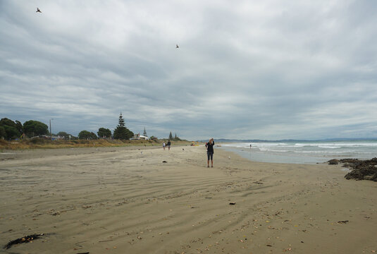 A woman taking pictures at Bream beach in Mangawhai New Zealand.