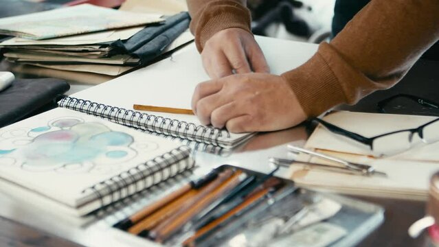 The artist's hands are working on his sketch. He corrects the lines with an eraser and continues to draw in pencil. Close-up shot