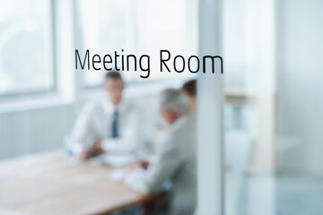 The meeting is in session. Closeup of a glass door reading meeting room with business people...