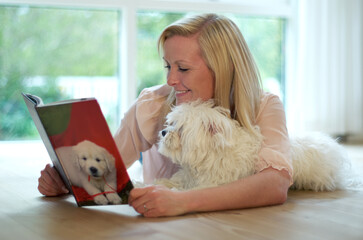Learning all about you. A young woman reading a book about dogs while cuddling her dog.