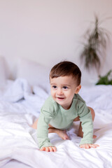Fototapeta premium cheerful baby in a green cotton bodysuit is lying on his stomach on a white bed