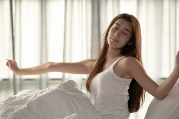 Fototapeta na wymiar Woman stretching in bed after wake up in the morning on big window background in bedroom