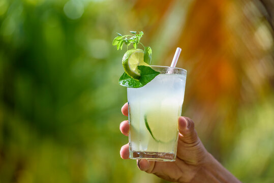 Brazilian drink caipirinha. Hand holding a caipirinha drink with blurred foliage in the background.