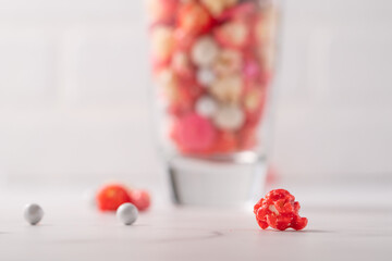 Colorful red and pink candied popcorn with mixed candies in glass cup
