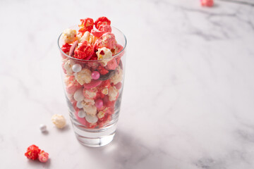 Colorful red and pink candied popcorn with mixed candies in glass cup