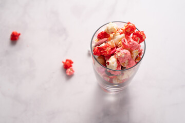 Colorful red and pink candied popcorn with mixed candies in glass cup