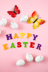 Easter eggs, colorful letters and butterflies on a pink background. Happy easter concept. Festive background, flat lay.