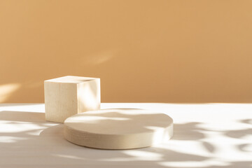 Wooden geometric podium for product demonstration. 3d round and square shapes on white and beige background with floral shadow. Stands for presentation of cosmetics