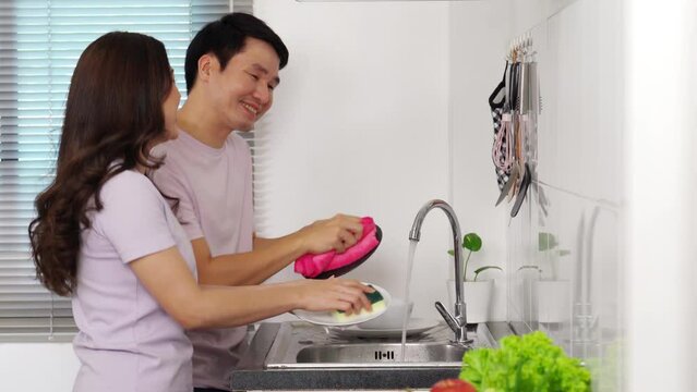 cheerful young couple dancing while washing dishes together in the sink in the kitchen at home