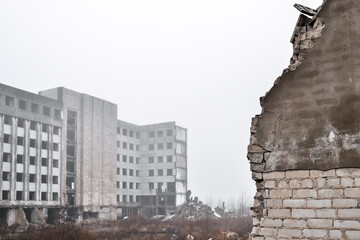 A broken brick wall in close-up against the ruins of a building and a gray sky in the fog. Background