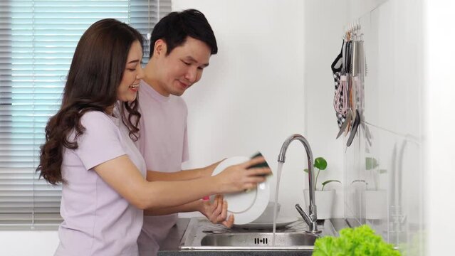 happy young couple washing dishes together in the sink in the kitchen at home