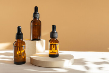 Mock-up of amber-colored glass bottles with dropper lid on beige background with floral shadow. Containers with facial serum close-up on geometric 3d wooden podium. Concept of beauty industry