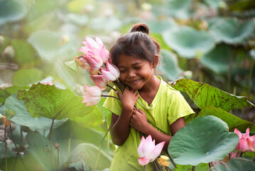 A girl with a perfect smile holding a lotus flower and looking at the camera. Portrait of a young girl smiling happily. - obrazy, fototapety, plakaty