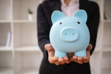 A young businessman or investor holds a blue piggy bank in her hand. The piggy bank is an idea for saving or accumulating assets for investment or for retirement.