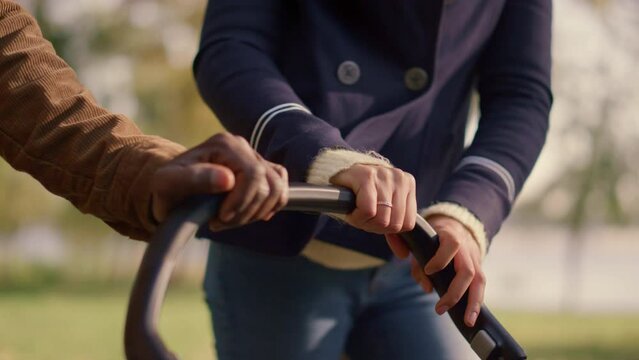 Parents hands on stroller pushing baby carriage closeup. Happy married couple.