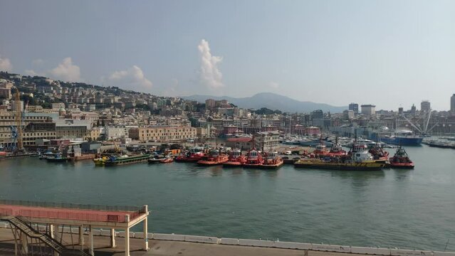Port of La Spezia, Cinque Terre, Italy. Tugboat is moving backward to position in a gap between anchored boats. Horizon behind with hills full of houses and green areas. Clear sky with a couple clouds