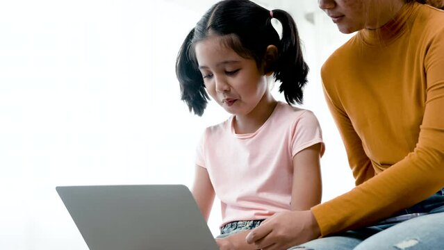 4K, 50 fsp Two young Asian girls sit on the bed in the bedroom, sister teaching sister to play laptop computer..