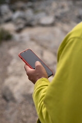 against the background of a rocky terrain, a phone in an orange case is in the hands of a young man. close-up and selective focus. a pistachio-colored sweatshirt. traveling in nature