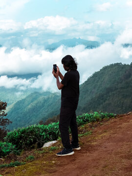 A young man taking a photo of a beautiful scenic tourist location using a mobile phone.