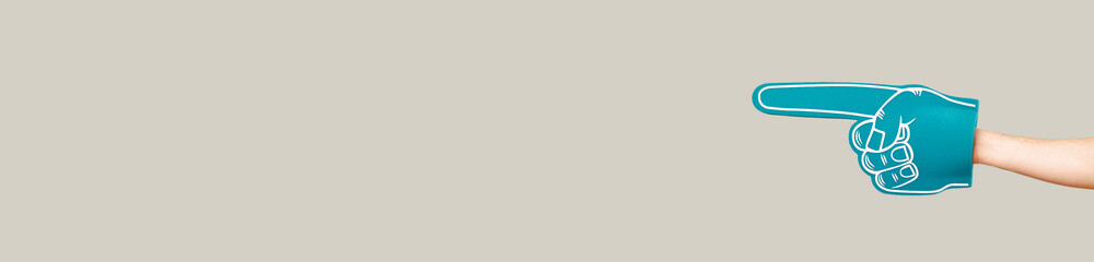 A male hand is wearing blue fan foam glove over panorama grey background.