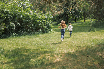 Naklejka na ściany i meble Children running after each other in blooming park on a sunny summer day.