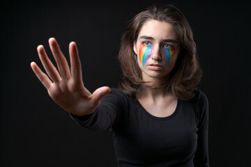 Flag LGBT lizbian woman with rainbow tears on her cheek defends herself with her hands in front of...