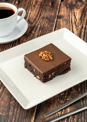 Walnut and dark chocolate brownie on a white porcelain plate on wooden table