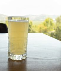 yellow lemonade in a glass glass stands on a wooden table in a summer restaurant with a view of a hilly landscape