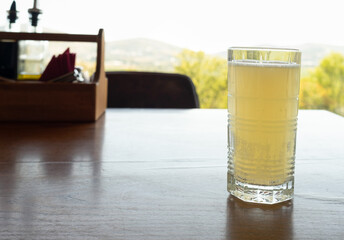 yellow lemonade in a glass glass stands on a wooden table in a summer restaurant with a view of a hilly landscape