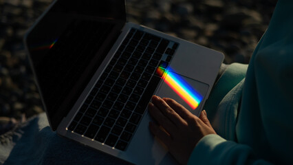 A woman is typing on a laptop. Rainbow light from a prism. 