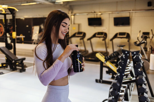 Beautiful young woman holding a plastic bottle of water at the gym. Portrait of a beautiful woman at the gym drinking water from the bottle - fitness concepts.