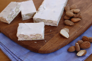 Traditional italian festive Torrone di Cremona with almonds cut in pieces on a wooden cutting board on table