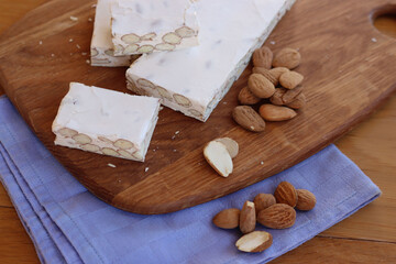 Fototapeta na wymiar Traditional italian festive Torrone di Cremona with almonds cut in pieces on a wooden cutting board on table