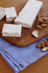 Traditional italian festive Torrone di Cremona with almonds cut in pieces on a wooden cutting board on table
