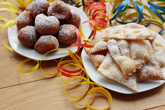 Traditional italian Crostoli ( also called  chiacchere, frappe, bugie, cenci, galani) and fritters called Frittelle with cream on wooden table with Confetti and coloful Carival decorations