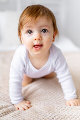 a small child girl learns to crawl on a bed in a bright room on cotton white linen, close-up portrait