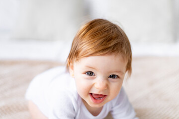 a close-up portrait of a laughing little baby girl in a bright room in white clothes at home on a bed, the concept of children's goods