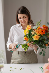 people, gardening and floral design concept - happy smiling woman or floral artist making bunch of flowers and cutting stems with pruning shears at home