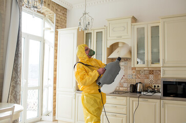 A man, an insect control specialist, in a yellow protective suit sprays the walls in the apartment,...