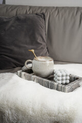 Blue bubble candle and cup of cappuccino on grey marble tray on white fluffy blanket, gray pillow