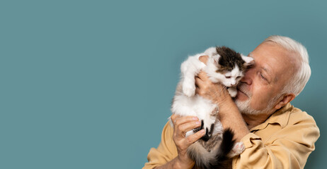 an elderly man holds a small kitten in his hands, love, care, light blue background, banner, space for text