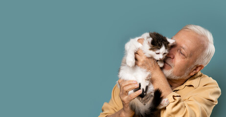 an elderly man holds a small kitten in his hands, love, care, light blue background, banner, space...