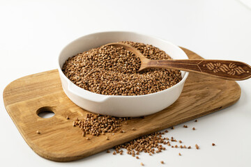 dry buckwheat groats in a white bowl on a wooden board with a wooden spoon, on a white background