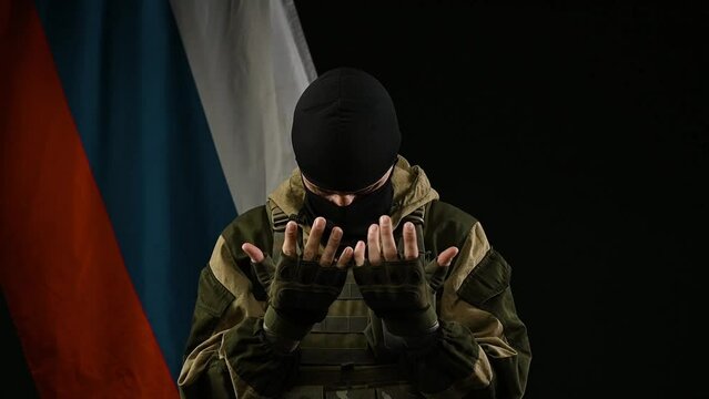 a Russian soldier on the background of a Russian flag with a balaclava regrets and prays