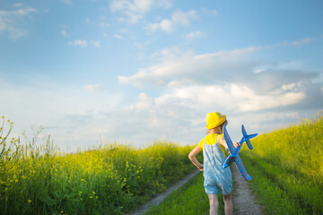 Girl in a yellow panama hat launches a toy plane into the field. Summer time, happy childhood, dreams and carelessness. Air tour from a travel agency on a trip, flight, adventure and vacation. 